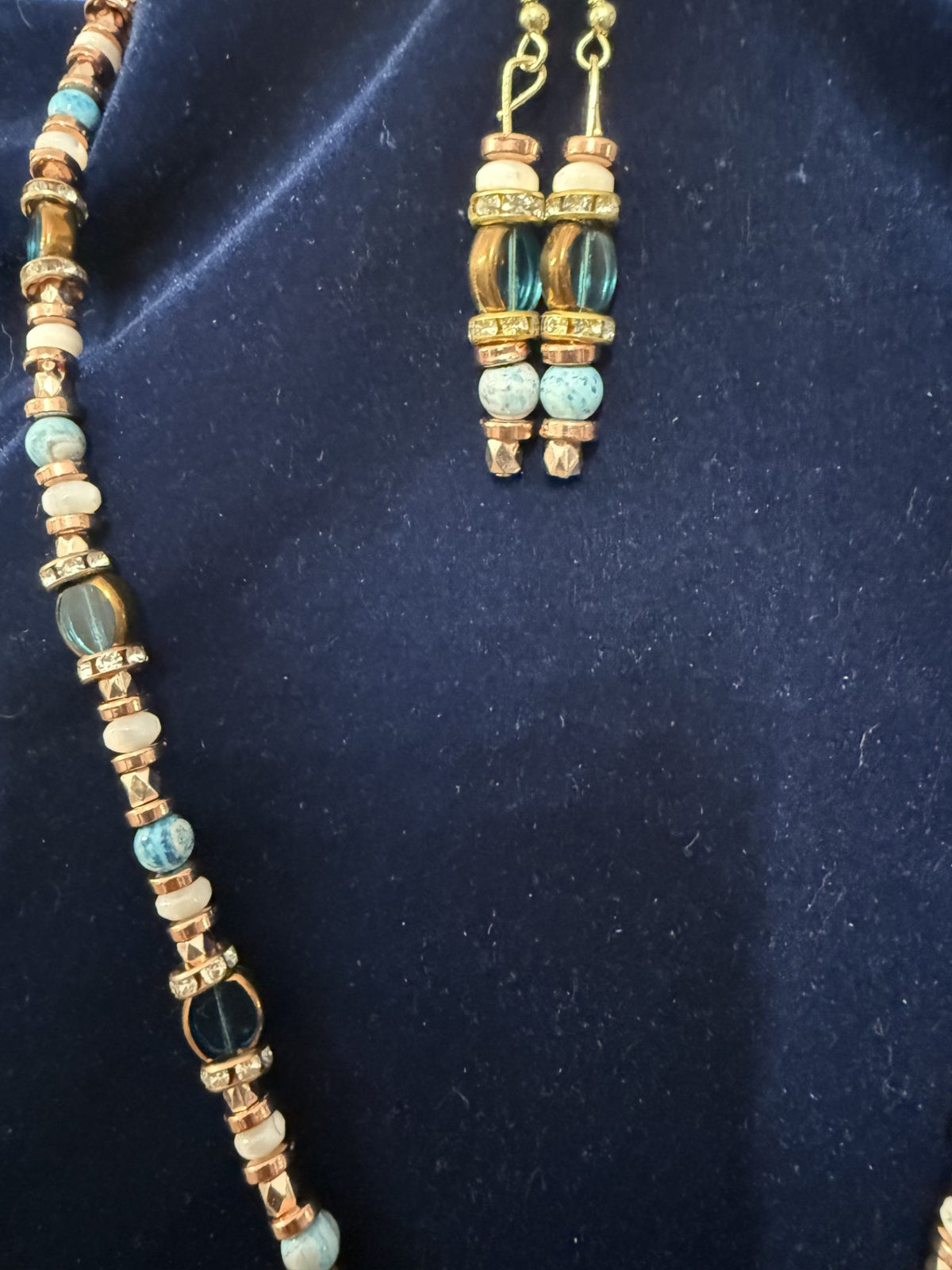 Necklace strand and earrings detail on navy velvet
