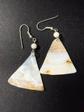 Pair of triangular mother-of-pearl dangle earrings with white bead accent on dark background