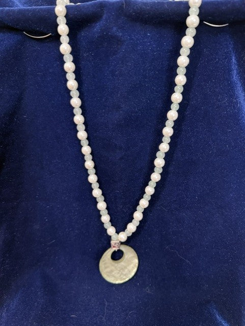 Full view of jade and freshwater pearl necklace with mother of pearl pendant on blue velvet
