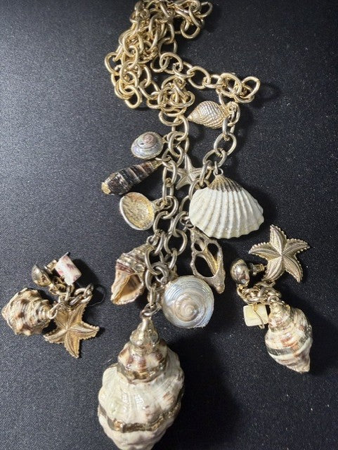 Full view of gold-leafed seashell charm necklace and earring set on dark background