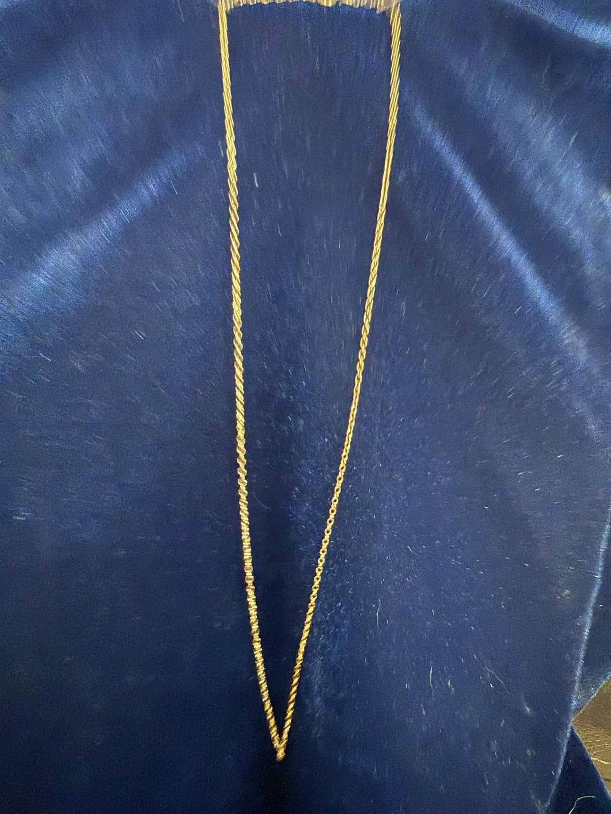 A delicate gold chain necklace draped in a V-shape against a dark blue textured fabric background.