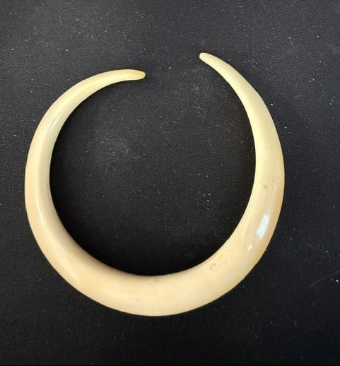 A cream-colored bone or ivory crescent-shaped earring with a silver metal band, shown alongside a matching small pointed bone pin on a black background.