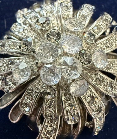 A vintage-style silver-toned brooch featuring a sunburst design with clear round and oval rhinestones, displayed on a dark blue velvet background.