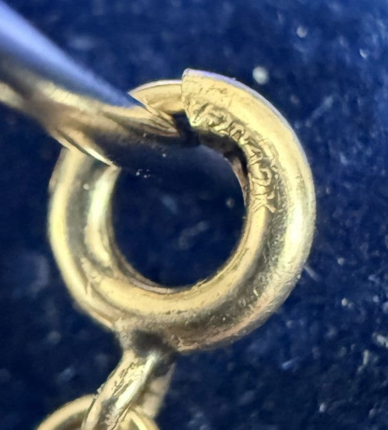 Close-up of a 12 kt GF metal clasp and chain extension on a dark blue textured surface, held by a metal probe.