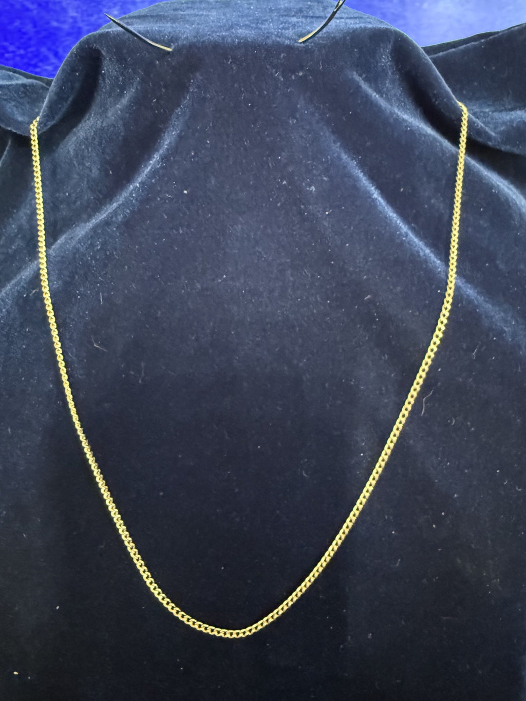 A gold chain necklace draped over a black velvet jewelry display bust against a blue background.