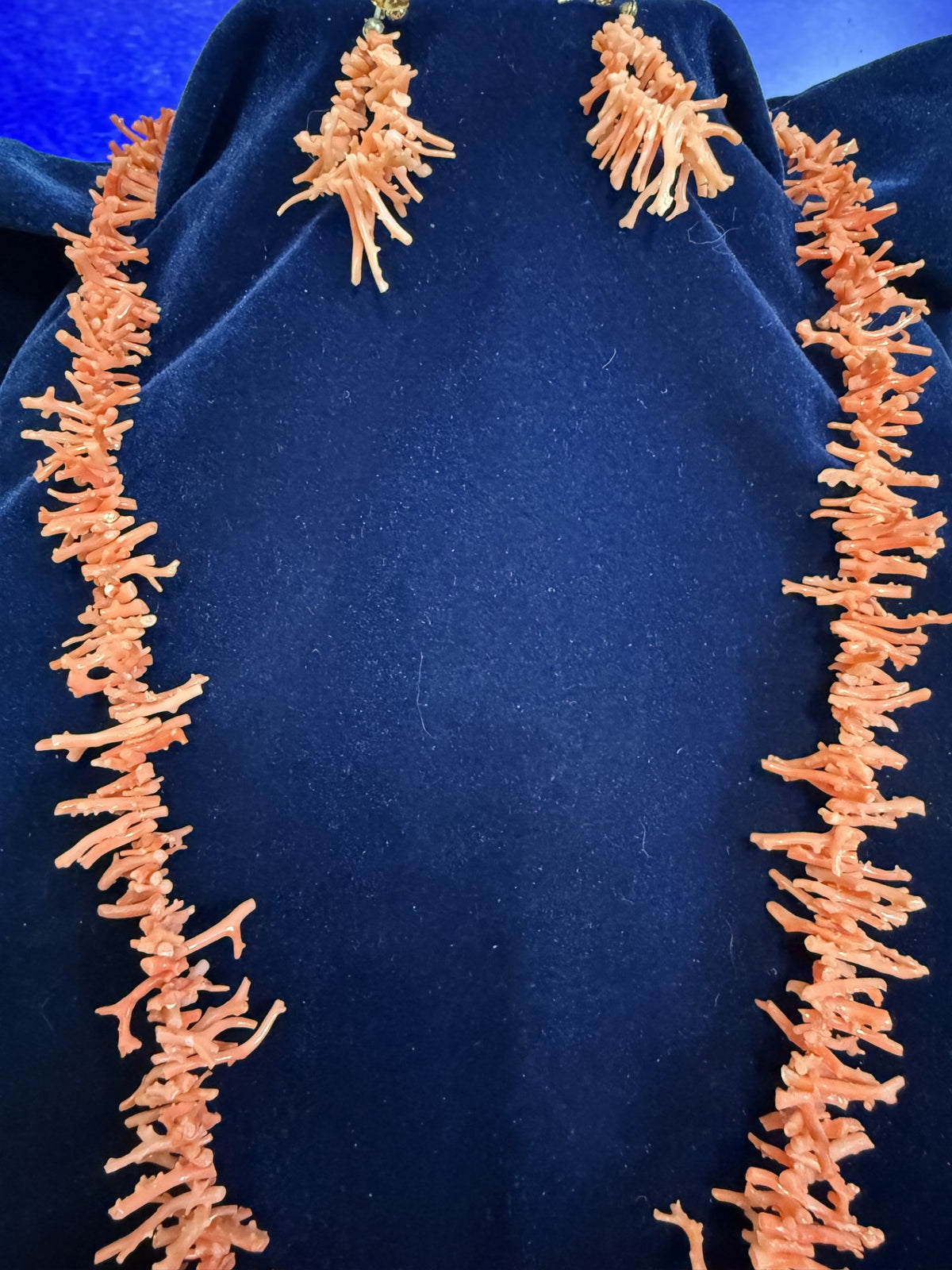 Orange coral necklace and matching drop earrings displayed on a dark blue velvet jewelry bust.