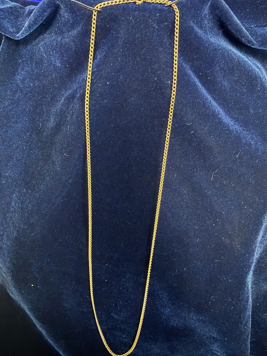 A gold chain necklace draped vertically over a dark blue velvet fabric background.