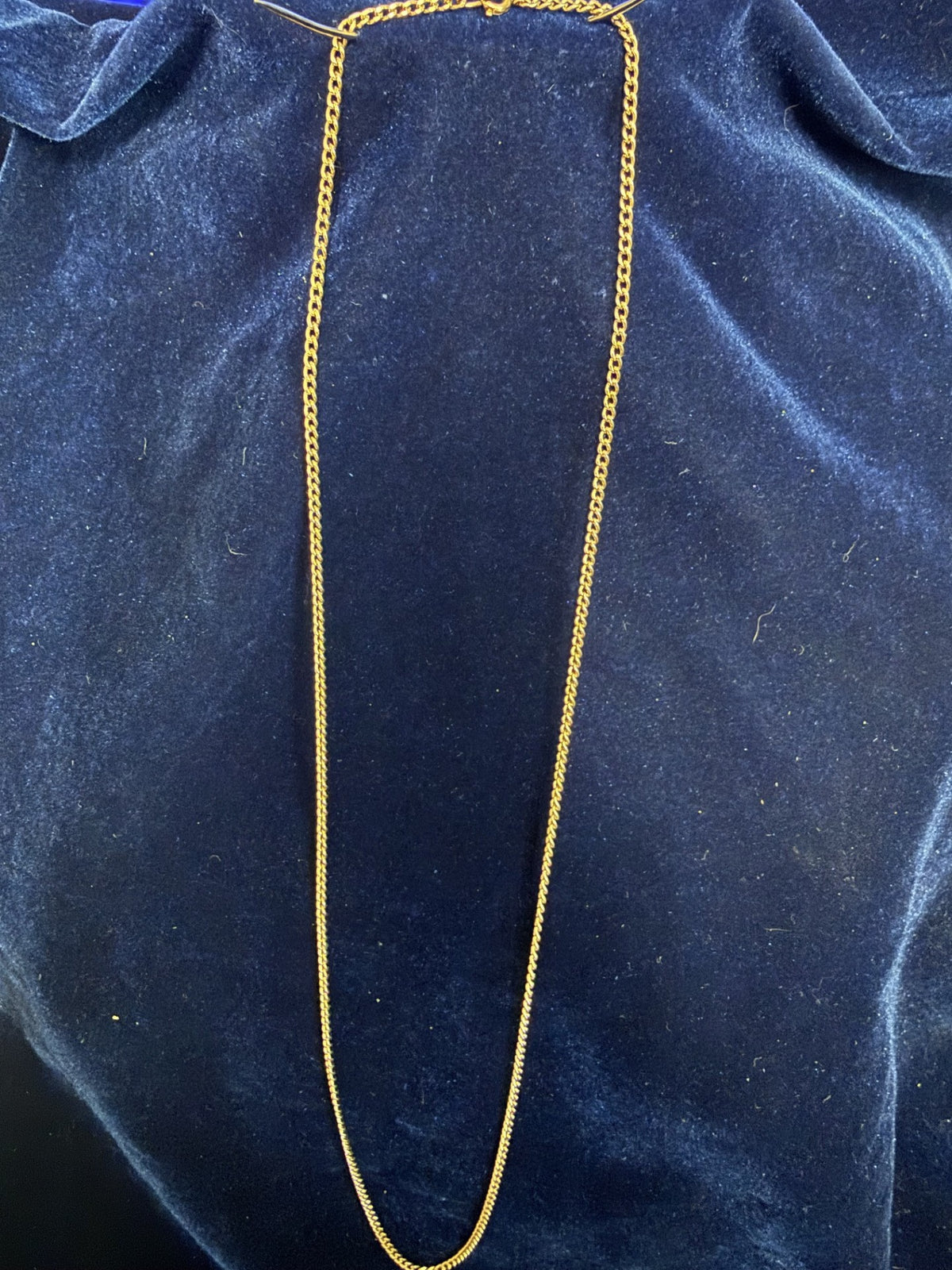 A gold chain necklace draped vertically over a dark blue velvet fabric background.