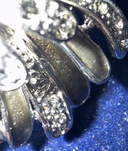 A close-up of a silver-toned claw-style ring with clear stones, resting on a textured blue surface.