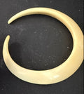 A close-up of a hand holding a gold-toned metal tool next to a large, cream-colored curved barbell earring on a black textured background.